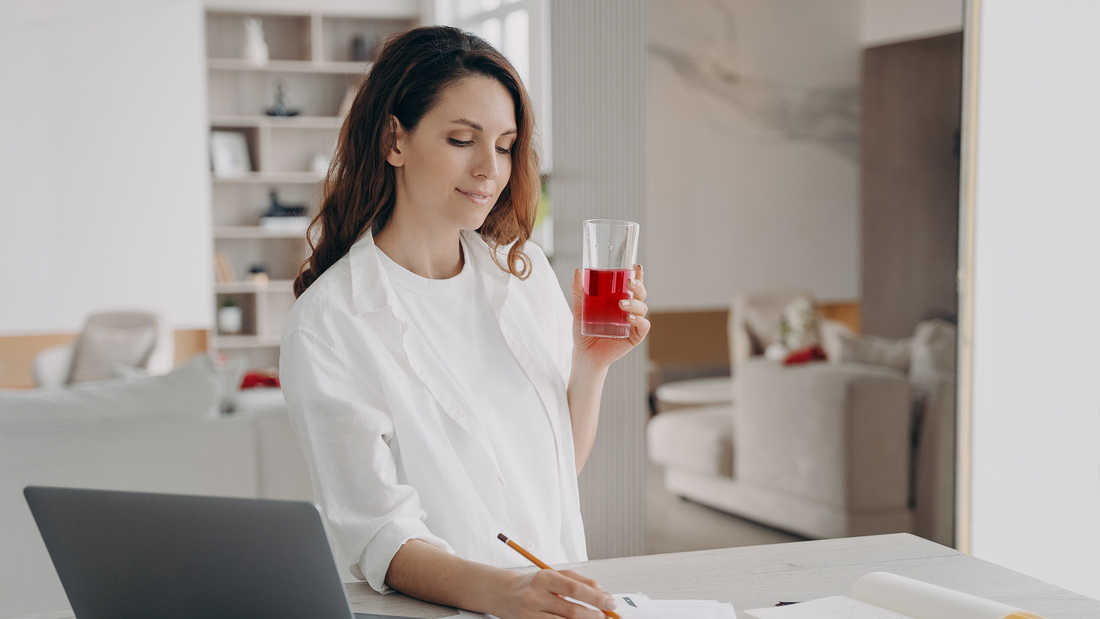 Kobieta pracująca w domowym biurze, trzymająca szklankę z napojem