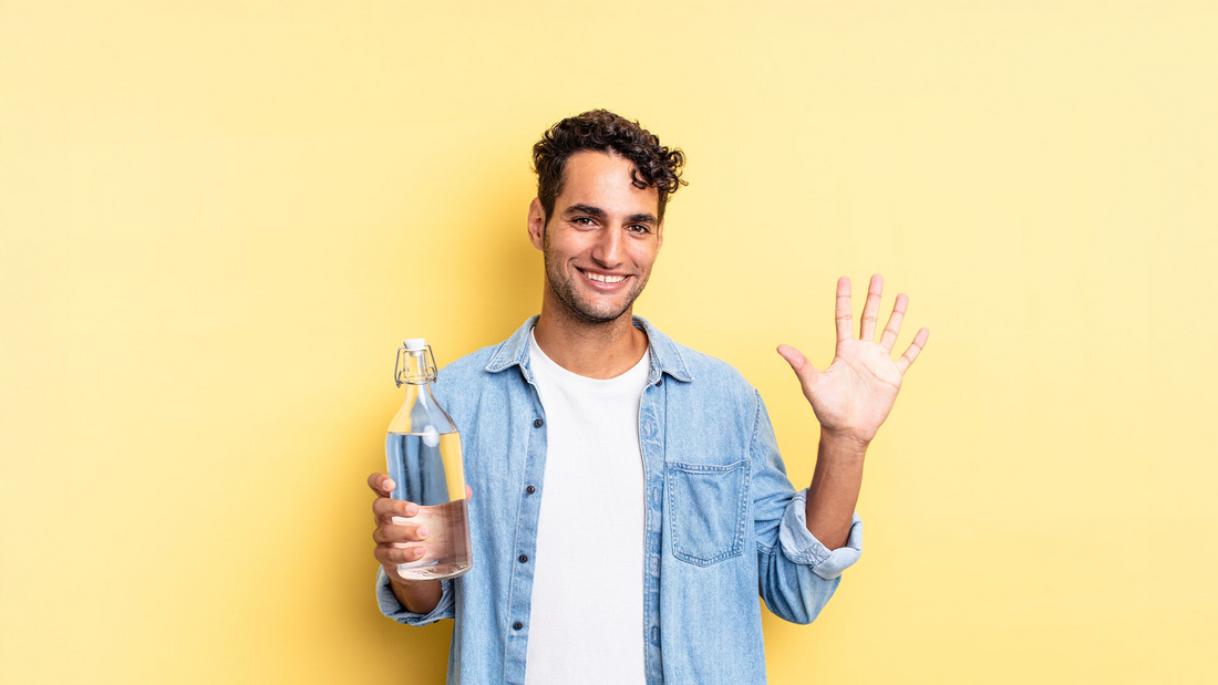 Mężczyzna na żółtym tle trzymający butelkę z wodą oraz otwartą dłoń