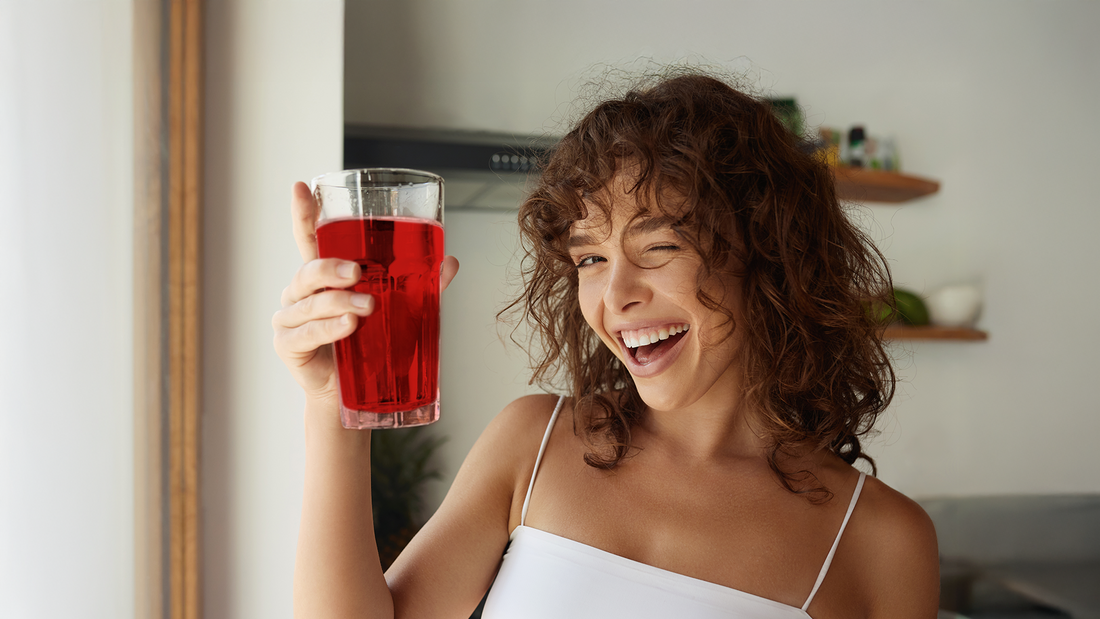 Uśmiechnięta kobieta trzymająca szklankę wypełnioną czerwonym napojem