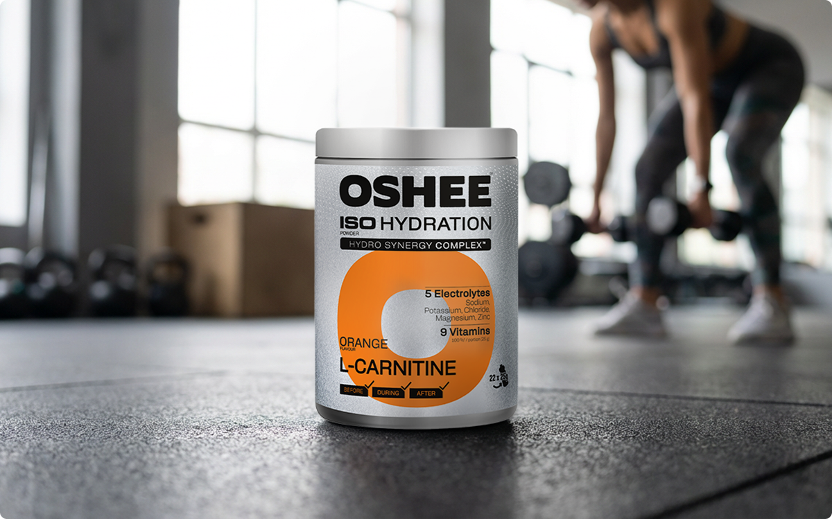 oshee l-karnityna pojemnik na siłowni, w tle ćwicząca kobieta