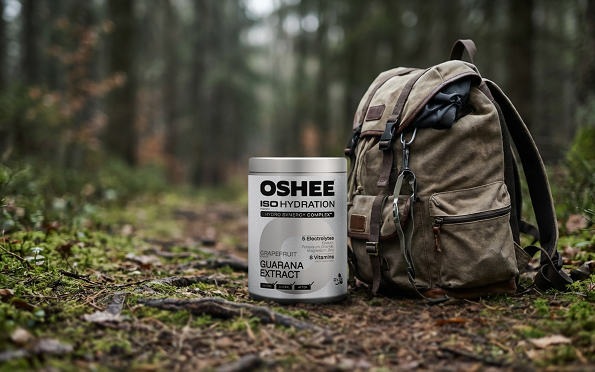 oshee grejpfrut guarana pudełko na tle lasu, obok stoi plecak 