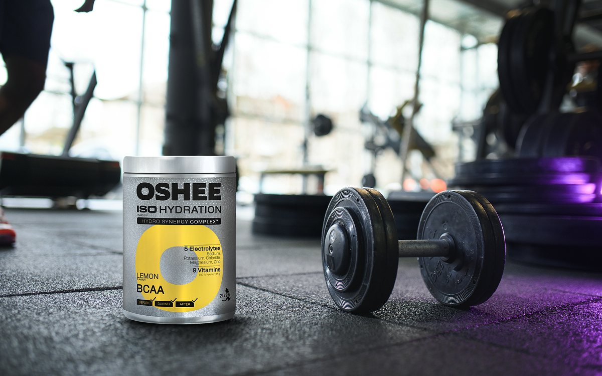 oshee lemon bcaa na tle siłowni, obok leży hantel do ćwiczenia